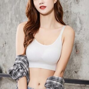 Model wearing a white comfortable bra with thin straps and a plaid shirt draped over her arm, against a textured wall.