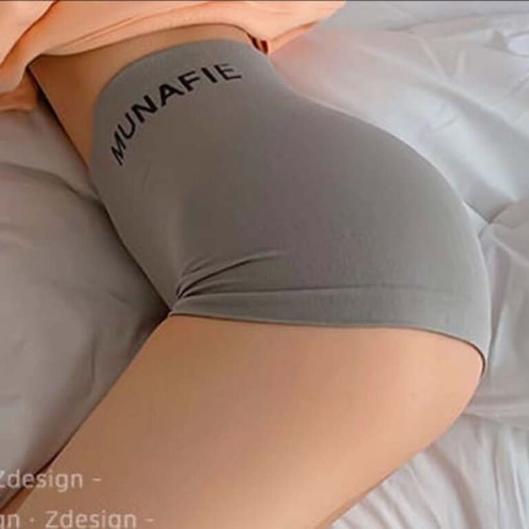 A close-up view of a person's lower body wearing gray shorts with 'MUNAFIE' written on the waistband, resting on a bed.
