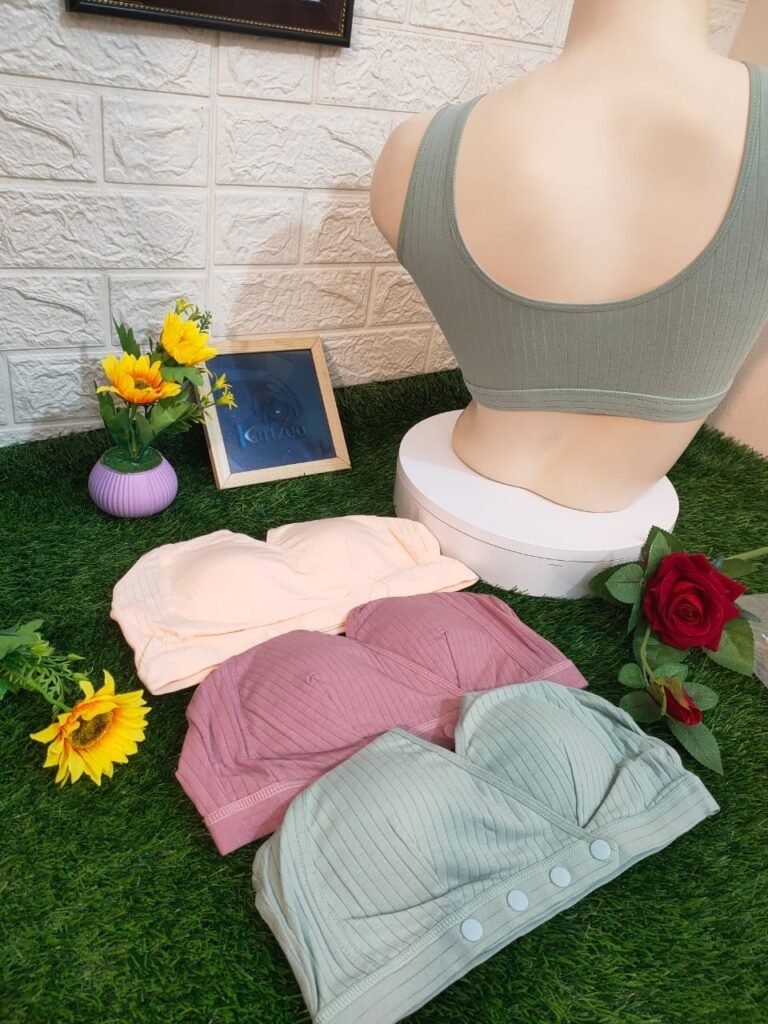 A display of three colored bras in pastel shades on a green grass-like surface, with a mannequin showcasing a green bra from the back, surrounded by flowers and a picture frame.